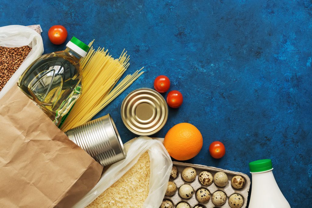 Oil in a bottle, pasta, canned food, cereals, eggs, milk, fruits and vegetables on a blue rustic background. Donation and charity. Top view, flat lay,copy space.