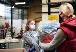 Volunteers And A Young Woman Donating Clothes In A Community Charity Donations Center.