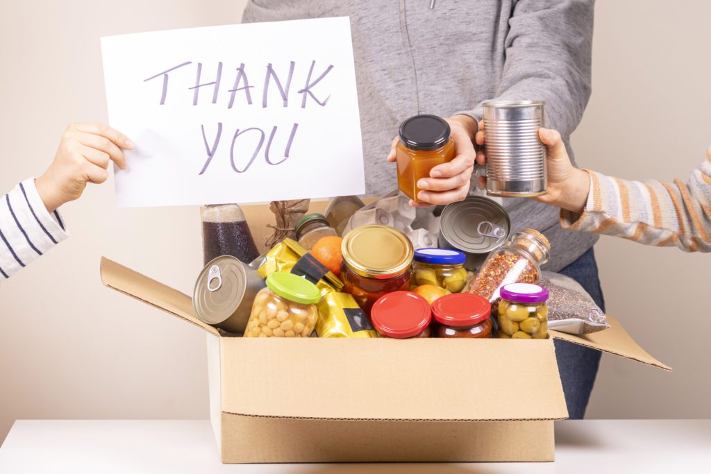 Volunteers Collect Grocery Products To food Donation Box And Holding Paper Sheet with Message saying Thank You.