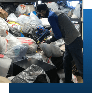 A Portrait Of A Man Segregating Clothes In A Pile Of Donated Items.